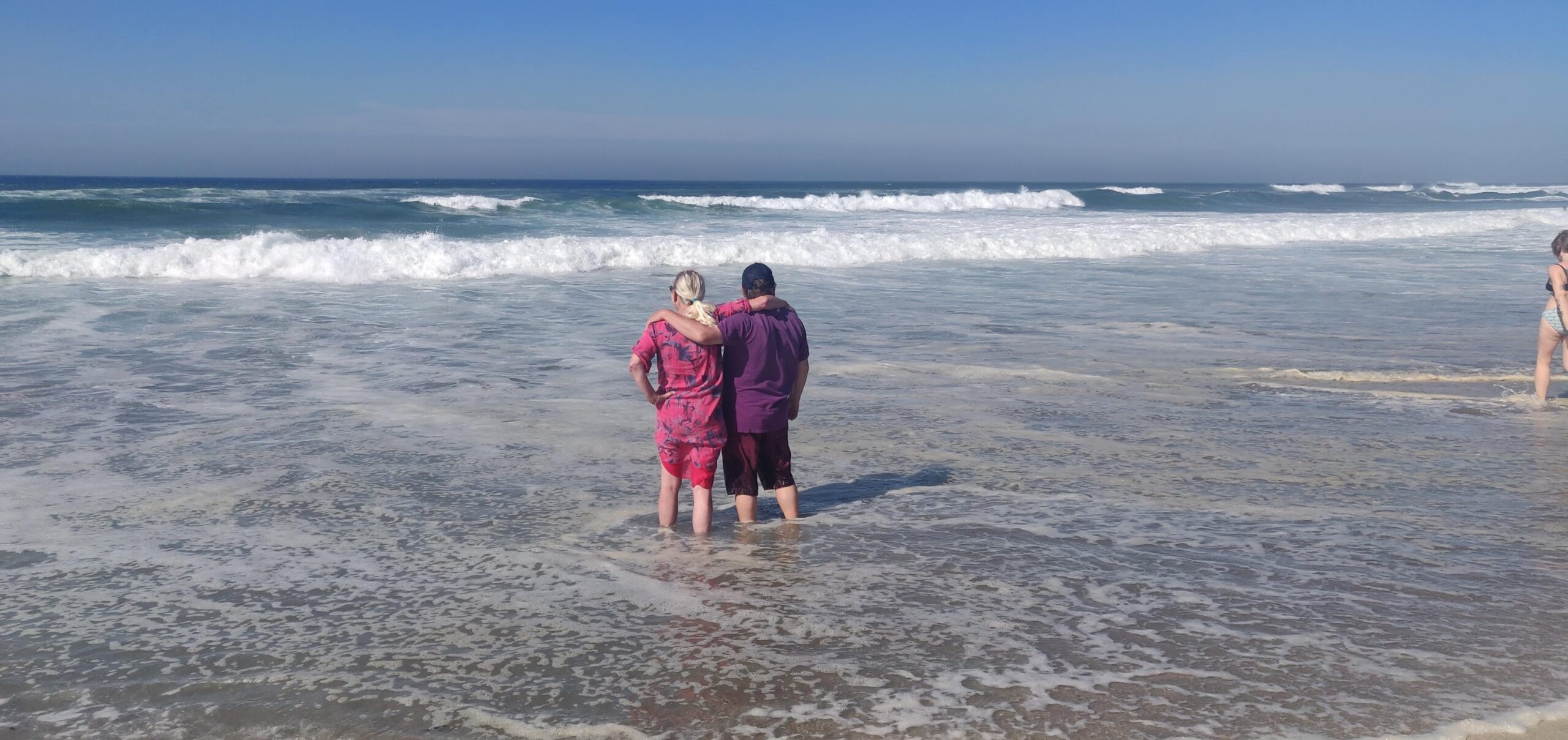 A couple stands, embracing, looking out to sea.